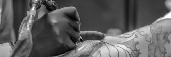 Artistic black and white photo capturing the detailed process of tattooing an arm.